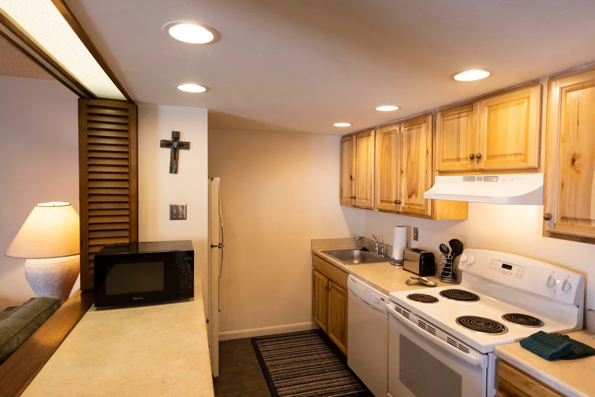 A warm, welcoming kitchen scene featuring wooden cabinets, stainless steel appliances, ample countertop space, and a lamp. The setup is ideal for preparing meals and entertaining, with a cozy and functional ambiance.
