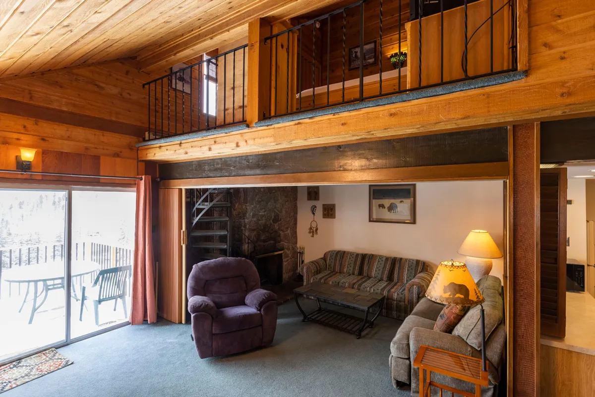 This image features a cozy living room with a sofa, recliner, coffee table, and a prominent fireplace. There is a staircase in the background, suggesting a spacious and dynamic interior. The warm lighting and comfortable furniture invite relaxation and group gatherings.
