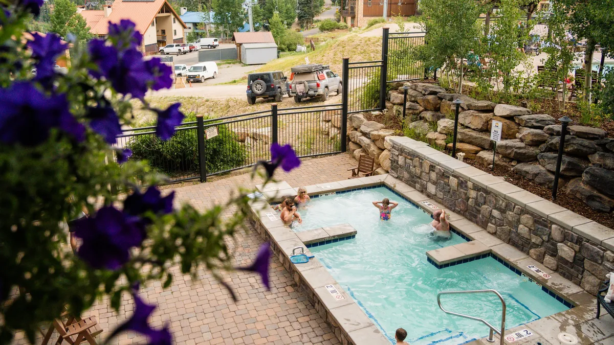 Taken from a different angle, this exterior shot focuses on a cheerful pool area bordered by blooming purple flowers and lush greenery. The setting invites guests to relax, socialize, and enjoy outdoor amenities after a day on the mountain.