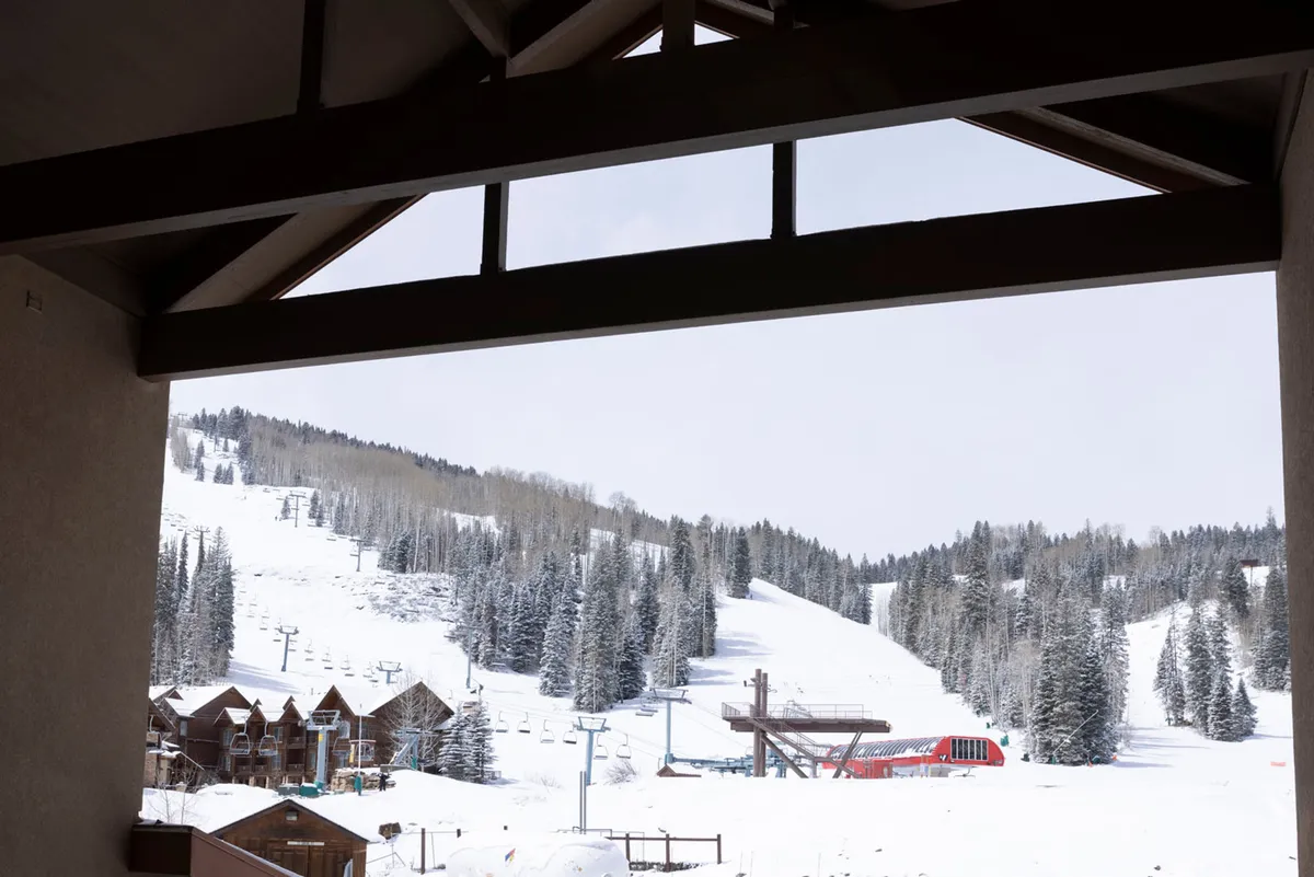 A picturesque winter scene featuring snow-covered slopes, a ski lift ready to whisk guests up the mountain, a dramatic mountain range in the background, and cozy chalets at the base. The inviting, serene atmosphere is accented by fresh snowfall and welcoming accommodations right at the edge of the action.