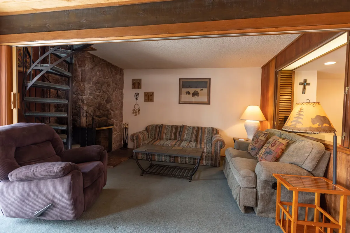 A stylish interior scene with a spiral staircase, stone wall, comfortable seating, wall art, and soft lighting from lamps. The arrangement encourages conversation and social activities, evoking an inviting and communal mood.